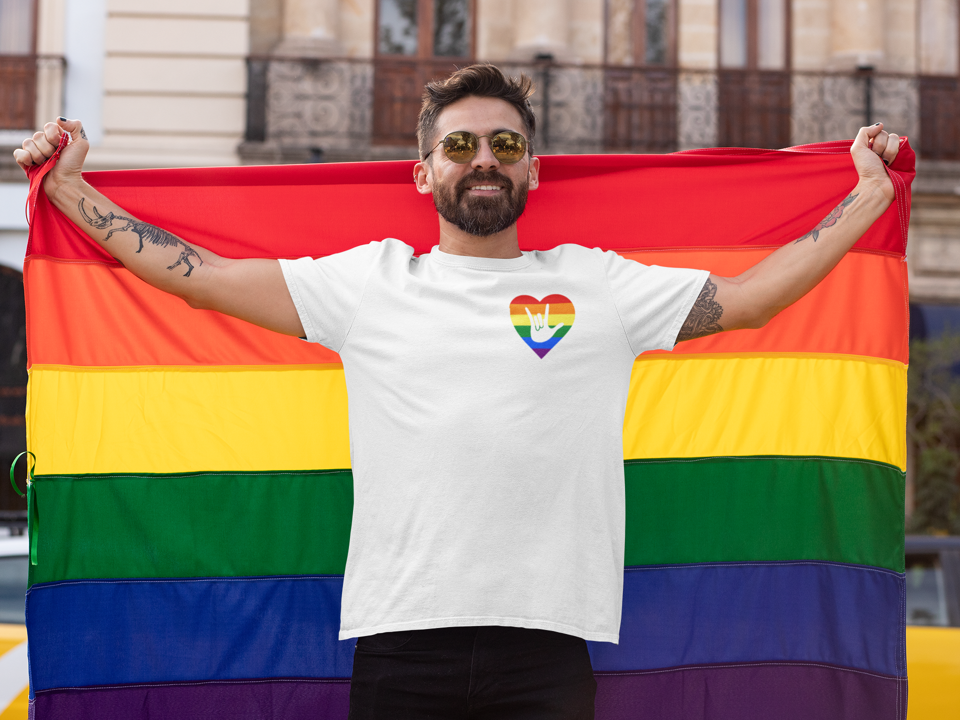 Man holding pride flag wearing white Signed with Pride t-shirt featuring rainbow heart with ASL sign, celebrating LGBTQ+ and Deaf community inclusion.