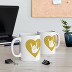 Two mugs with gold coloured heart designs featuring the ASL sign for I Love You embedded in them on a desk with office supplies.