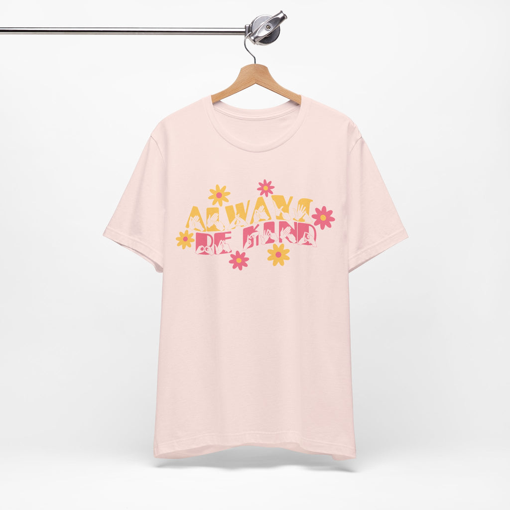 Front view of a soft pink T-Shirt with the phrase Always Be Kind in BSL fingerspelling and text combined with floral design, on a hanger against a white background