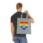 Man holding a Grey Tote Bag showing a Pride coloured heart and the iconic ASL I Love You sign embedded in it on a white background