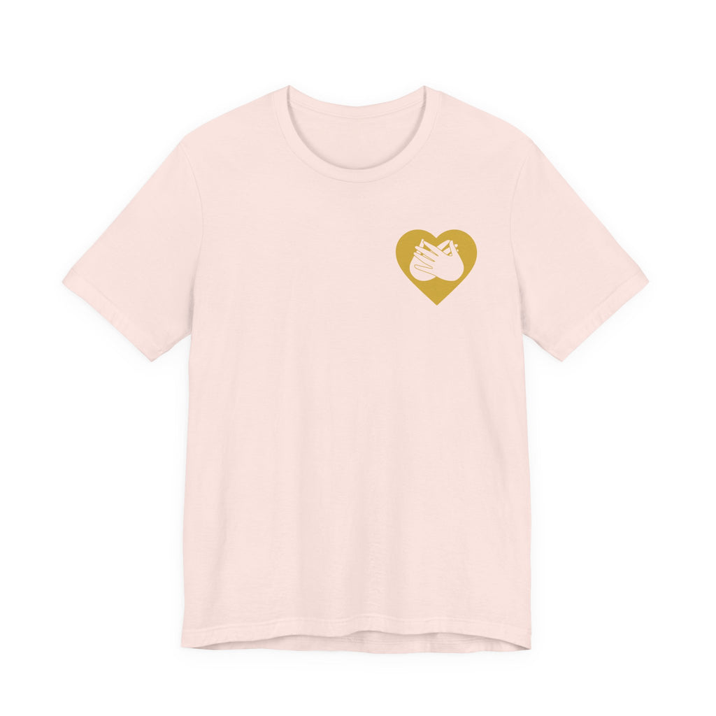 Front view of a soft pink T-Shirt showing a gold coloured heart and the iconic BSL Love sign embedded in it on the left side of the chest