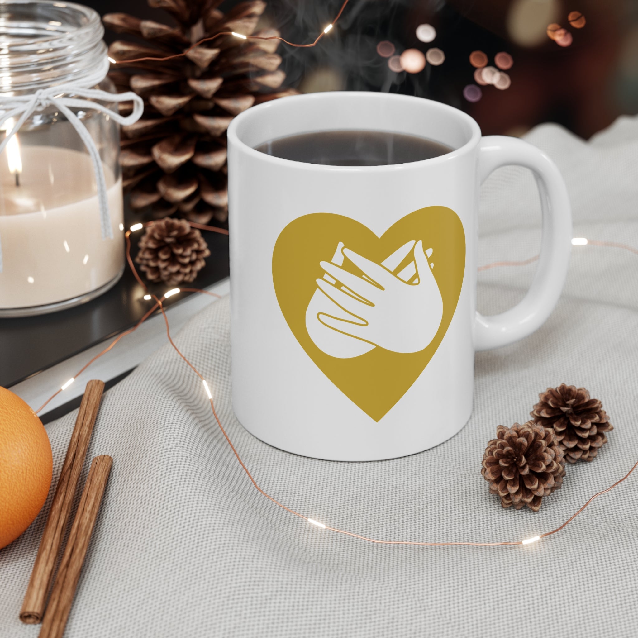 White mug with gold coloured heart design featuring the BSL sign for Love embedded in it on a table with decorative items.