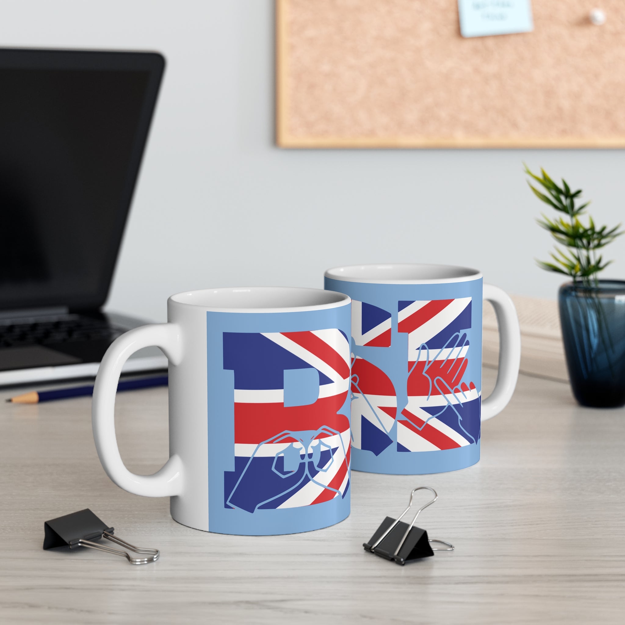 Two mugs with BSL Fingerspelling and text Union Flag design on a desk with office items.