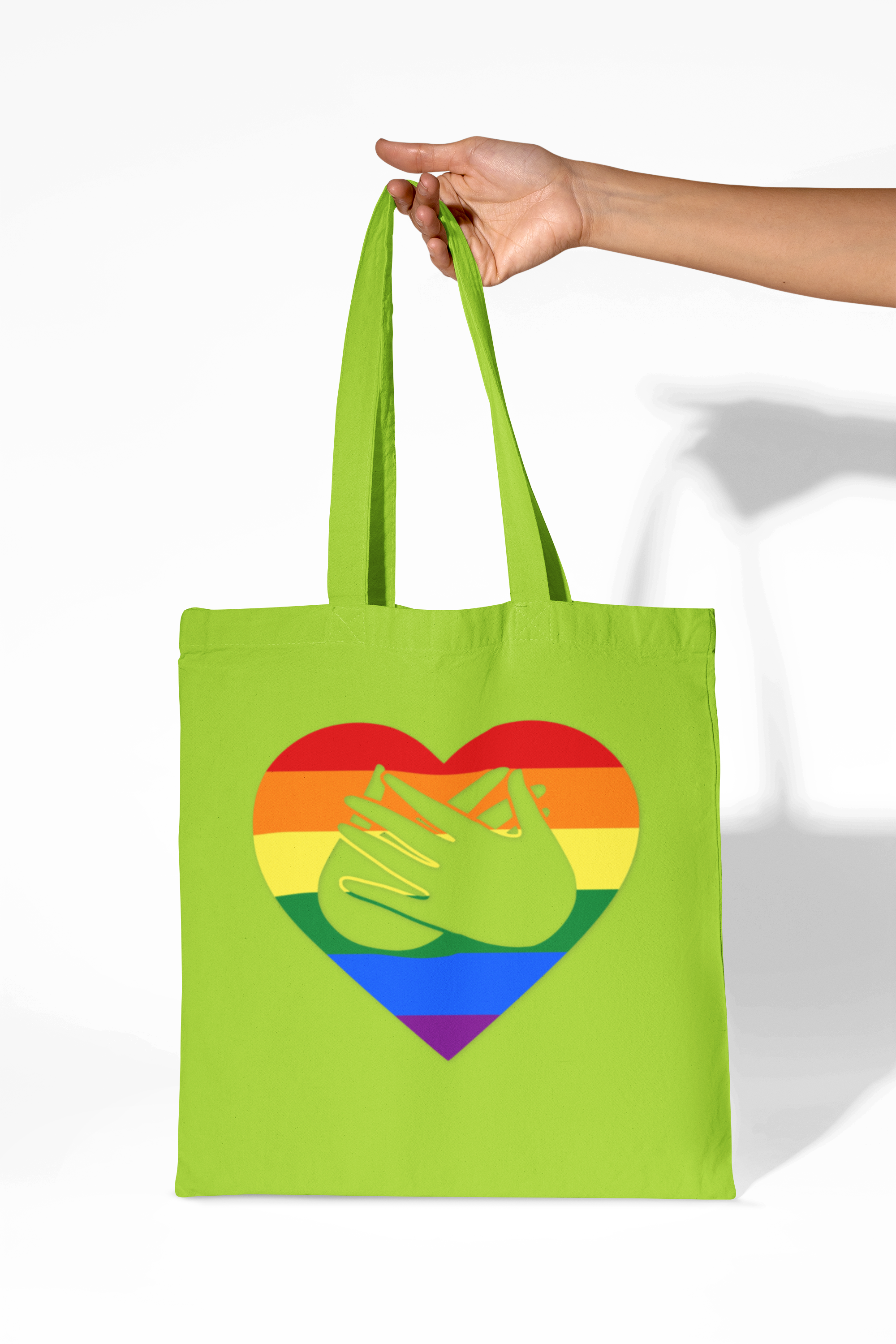 Lime Tote Bag showing a Pride coloured heart and the iconic BSL Love sign embedded in it, held by a hand on a white background
