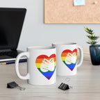 Two mugs with pride coloured heart designs featuring the BSL sign for Love embedded in them on a desk with office supplies.