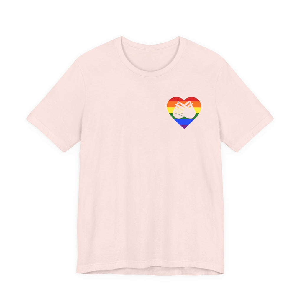 Front view of a soft pink T-Shirt showing a pride coloured heart and the iconic BSL Love sign embedded in it on the left side of the chest