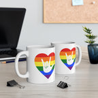 Two mugs with pride coloured heart designs featuring the ASL sign for I Love You embedded in them on a desk with office supplies.