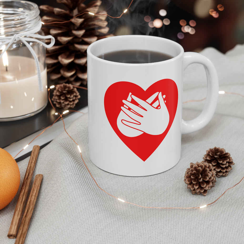White mug with red coloured heart design featuring the BSL sign for Love embedded in it on a table with decorative items.
