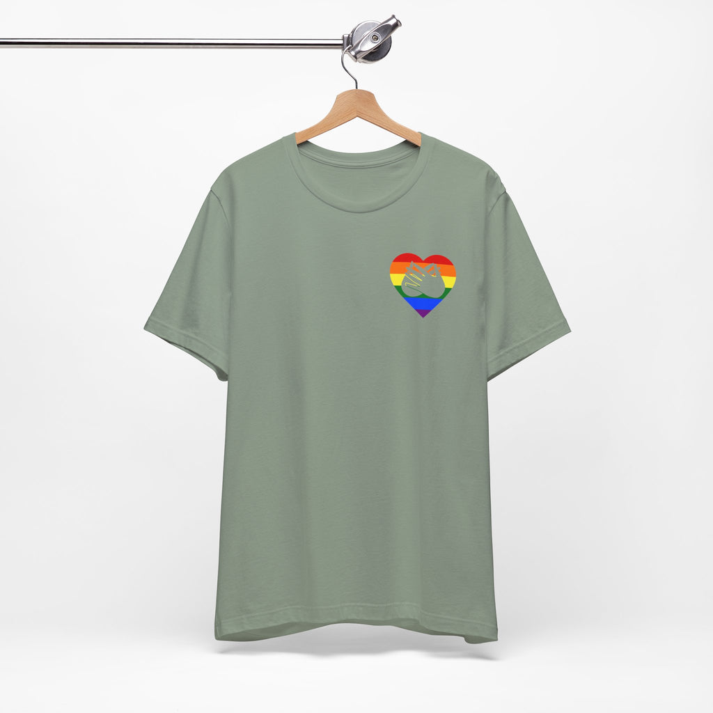Front view of a sage T-Shirt showing a pride coloured heart and the iconic BSL Love sign embedded in it on the left side of the chest, on a hanger against a white background