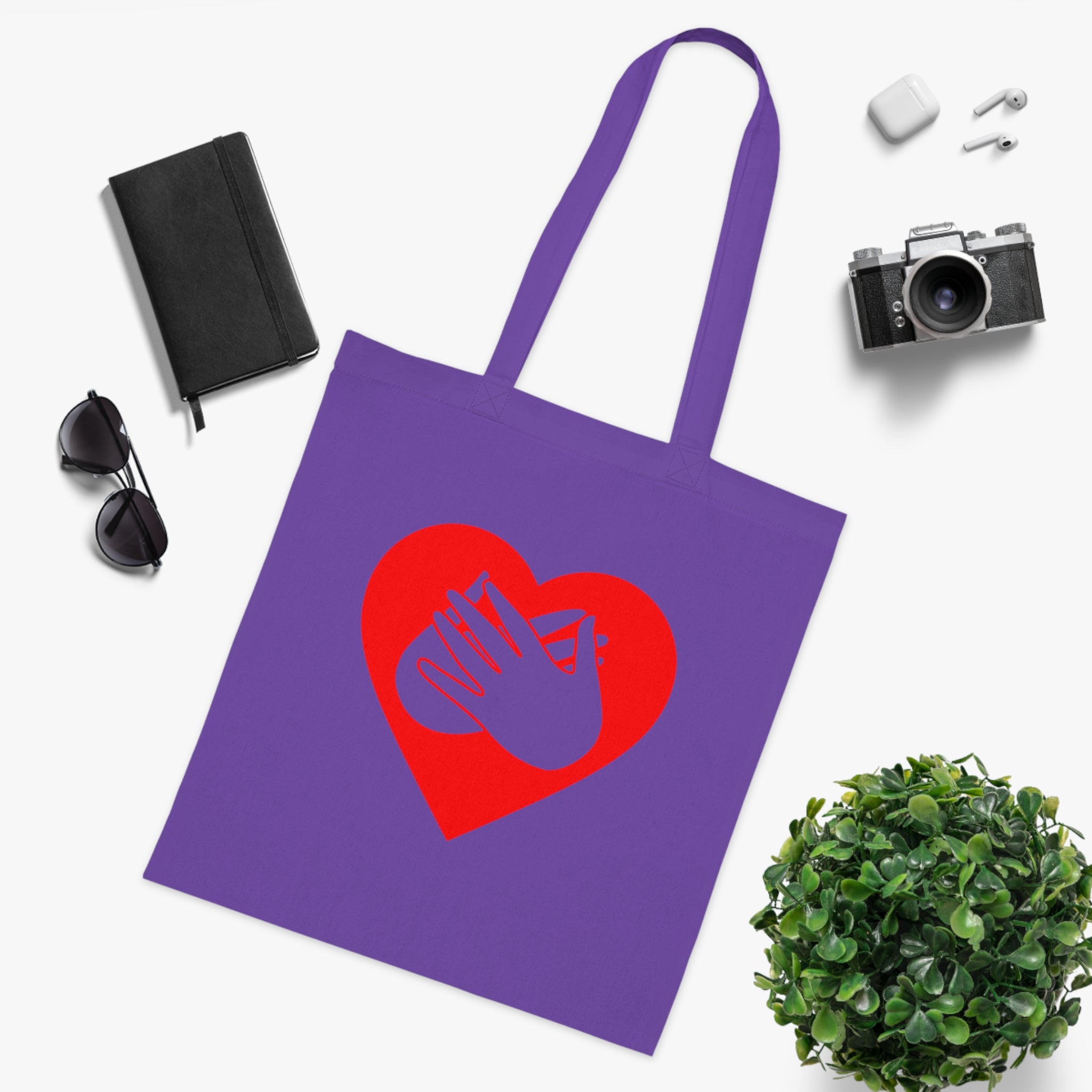 Lavender Tote Bag showing a red coloured heart and the iconic BSL Love sign embedded in it, surrounded by a black notebook, sunglasses, camera, and plant on a white background.