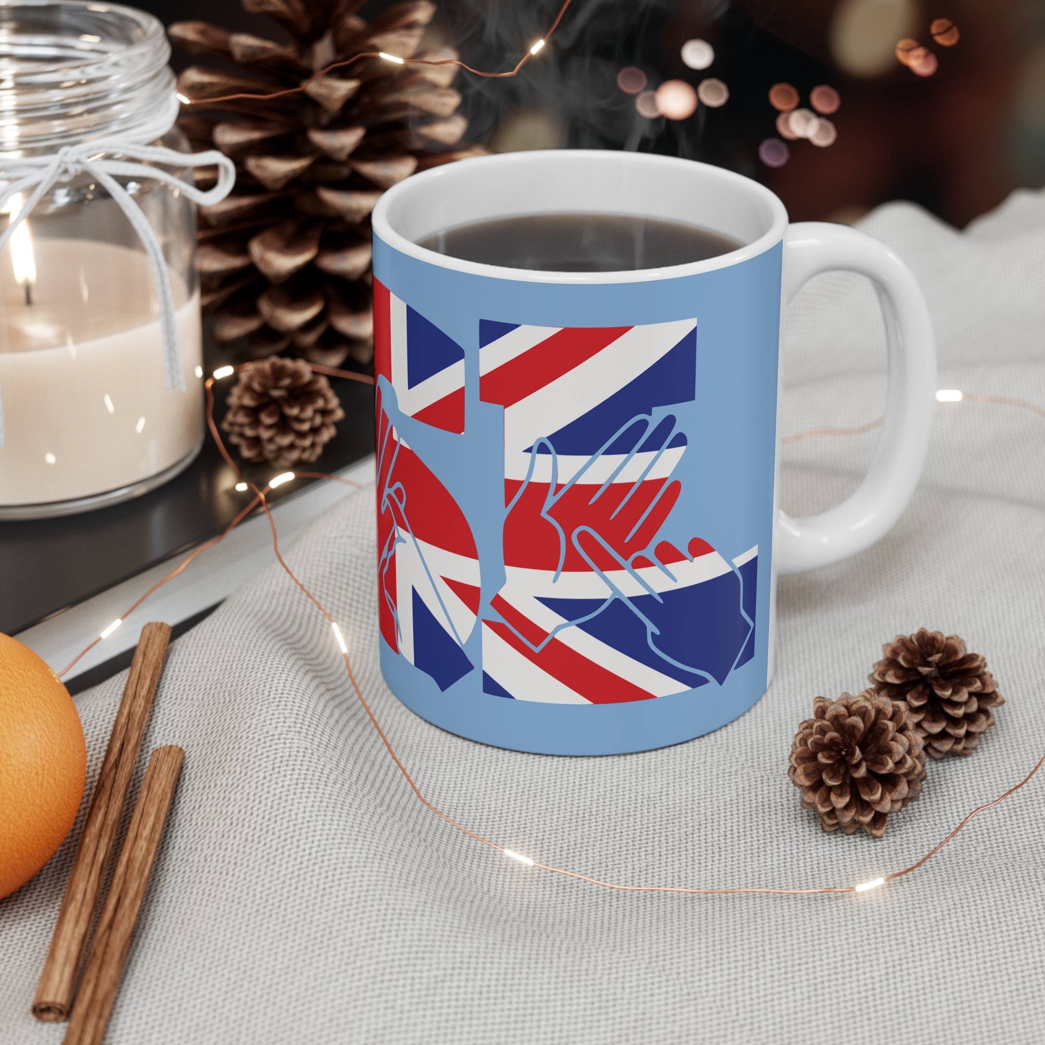 A  mug showing the B from the BSL acronym in fingerspelling and text with Union Flag colours on a blue background, placed on a table with decorative items