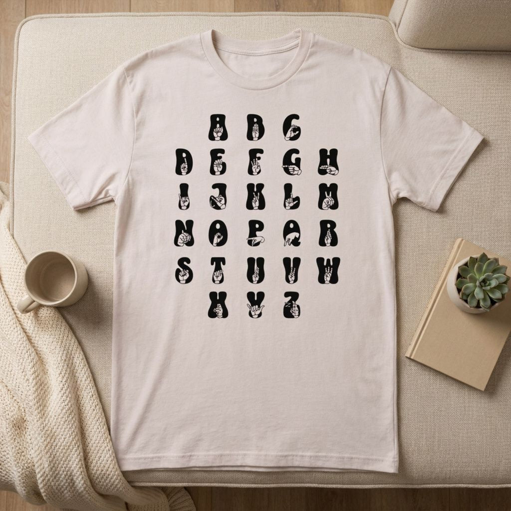 Front view of a ice grey t-shirt with ASL Alphabet - Black Fingerspelling & Text positioned on furniture.