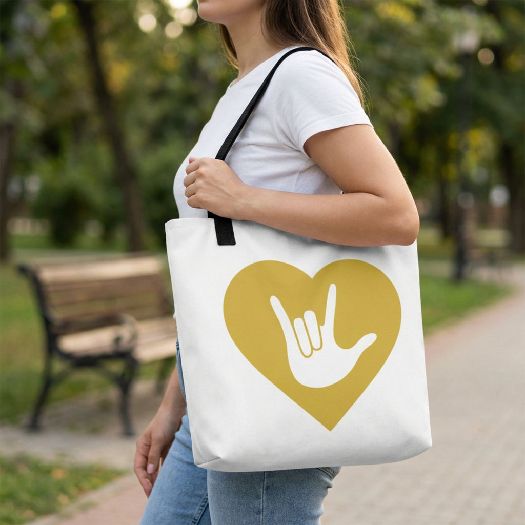 Person holding a tote bag with a heart and hand sign design in a park.