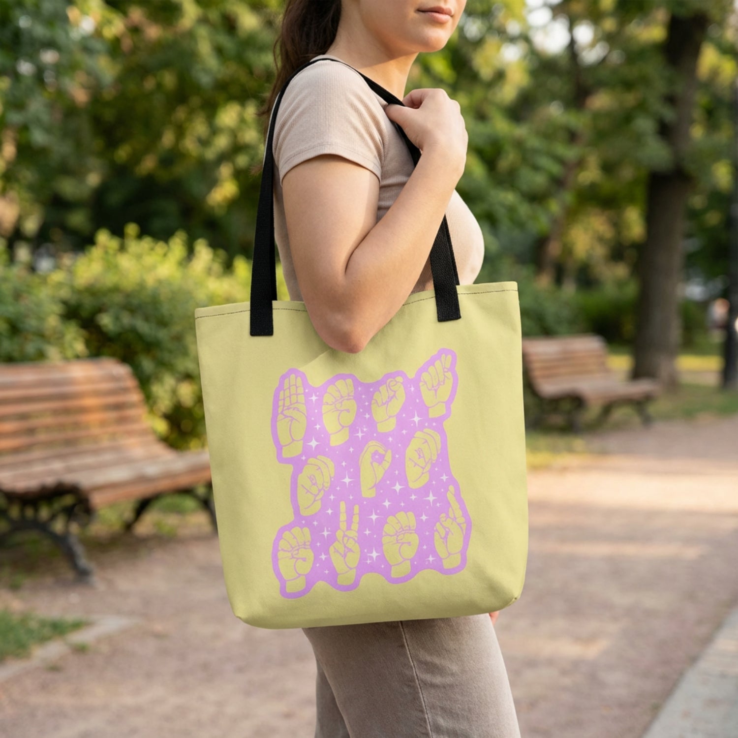 Person holding a green tote bag with a purple design in a park