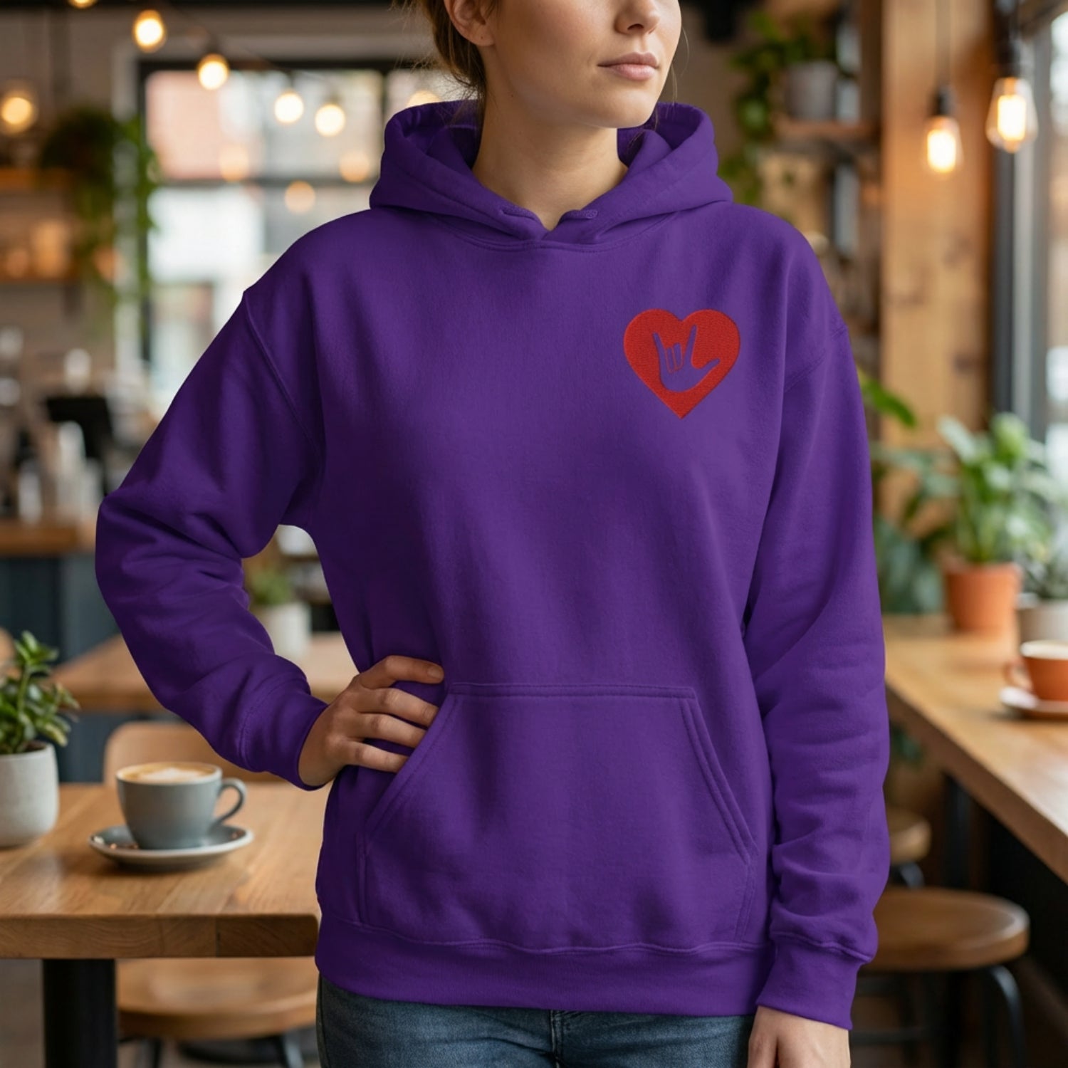 Person wearing a purple hoodie with a red heart design in a cafe setting
