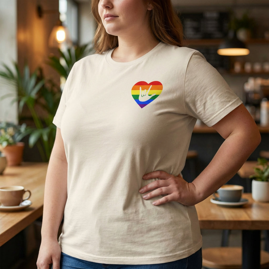 Person wearing a beige t-shirt with a pride rainbow heart design in a casual setting.