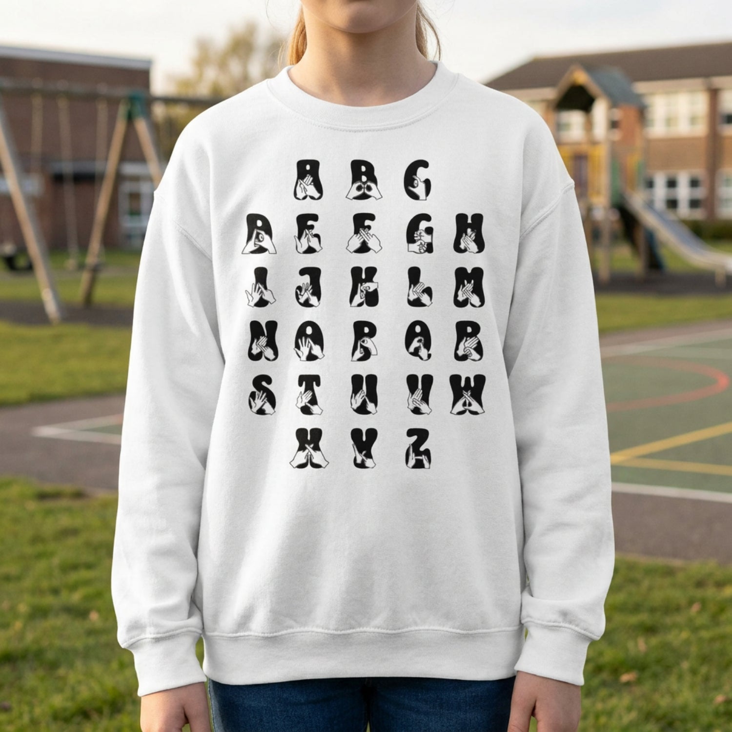 Person wearing a white sweatshirt with black alphabet letters outdoors.