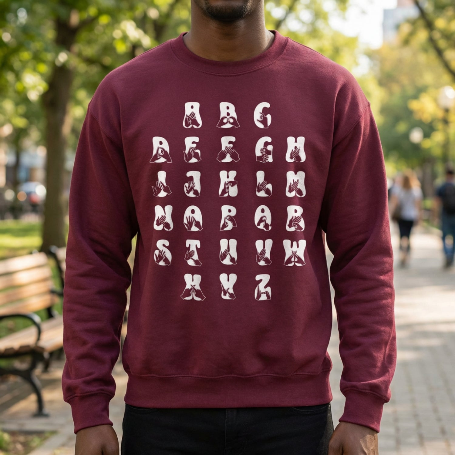 Person wearing a maroon sweatshirt with white alphabet letters outdoors.