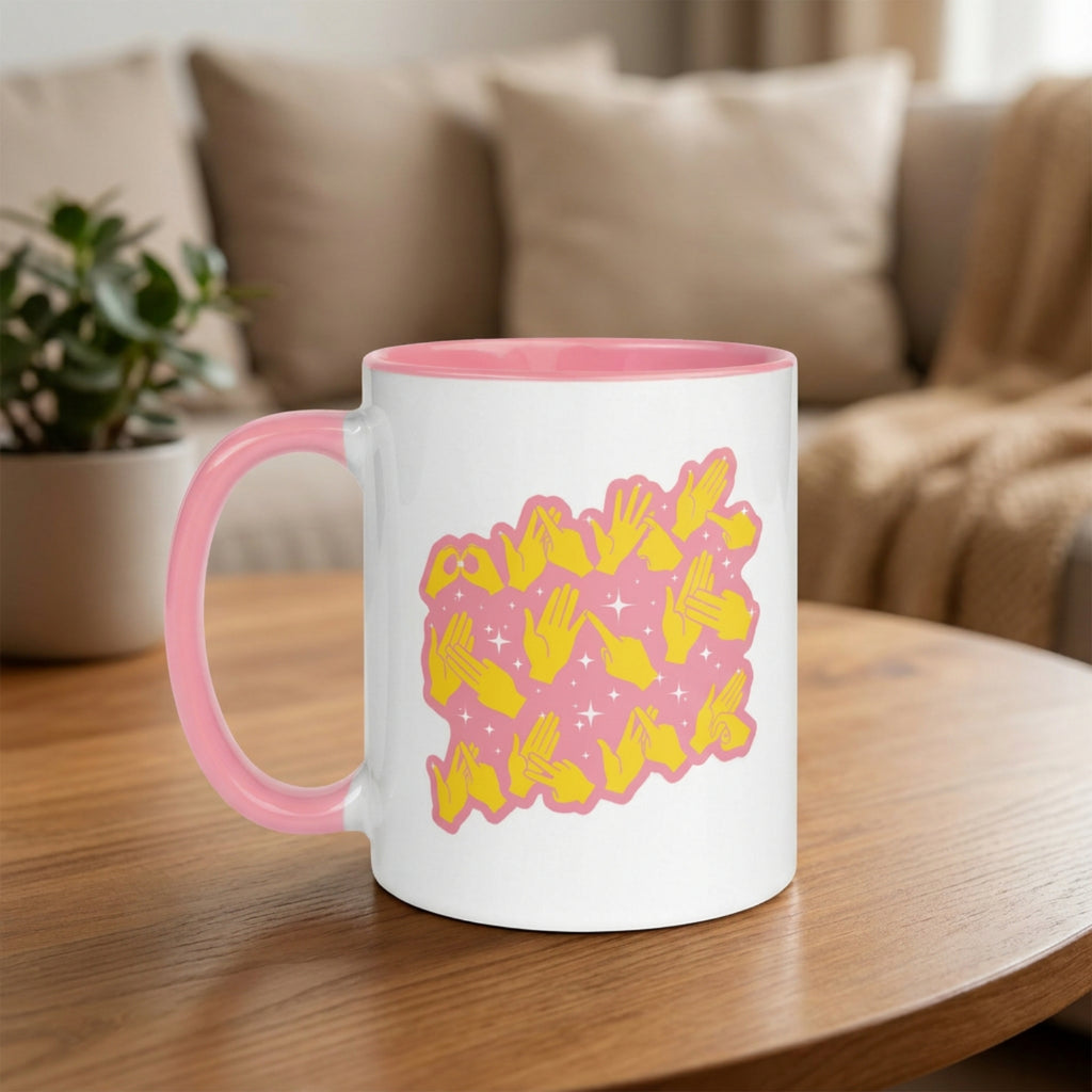 White mug with pink handle and yellow fingerspelling design on a wooden table