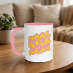 White mug with pink handle and yellow fingerspelling design on a wooden table