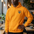 Person wearing a yellow hoodie with a rainbow heart design in a cafe setting