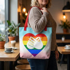 Person holding a tote bag with a rainbow heart design in a cafe setting