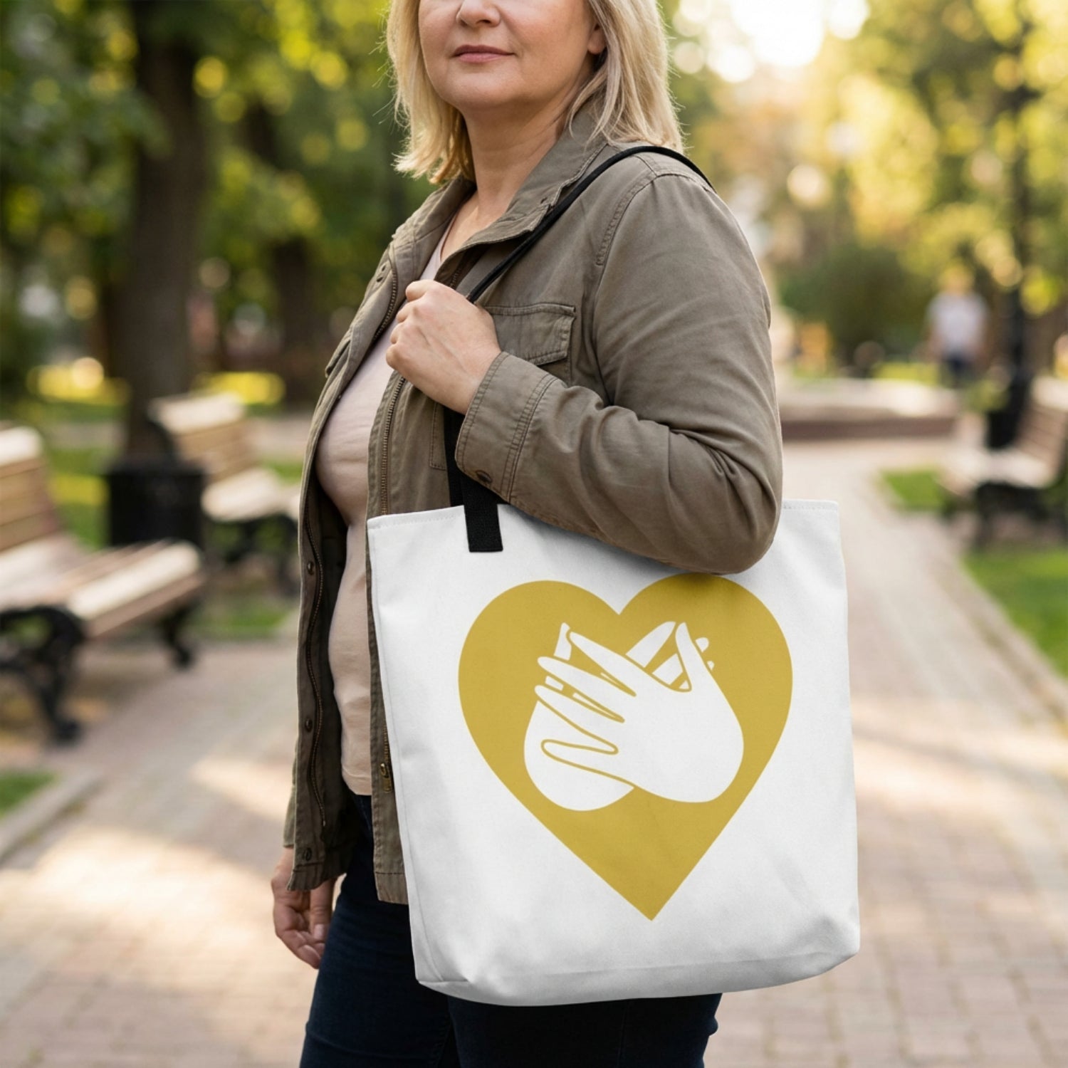 Woman holding a tote bag with a heart and hand design in a park.