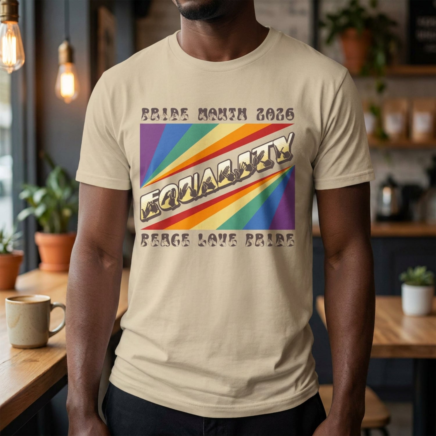 A person wearing a sand  t-shirt with pride rainbow spectrum of colours with the word Equality through the centre in BSL fingerspelling font