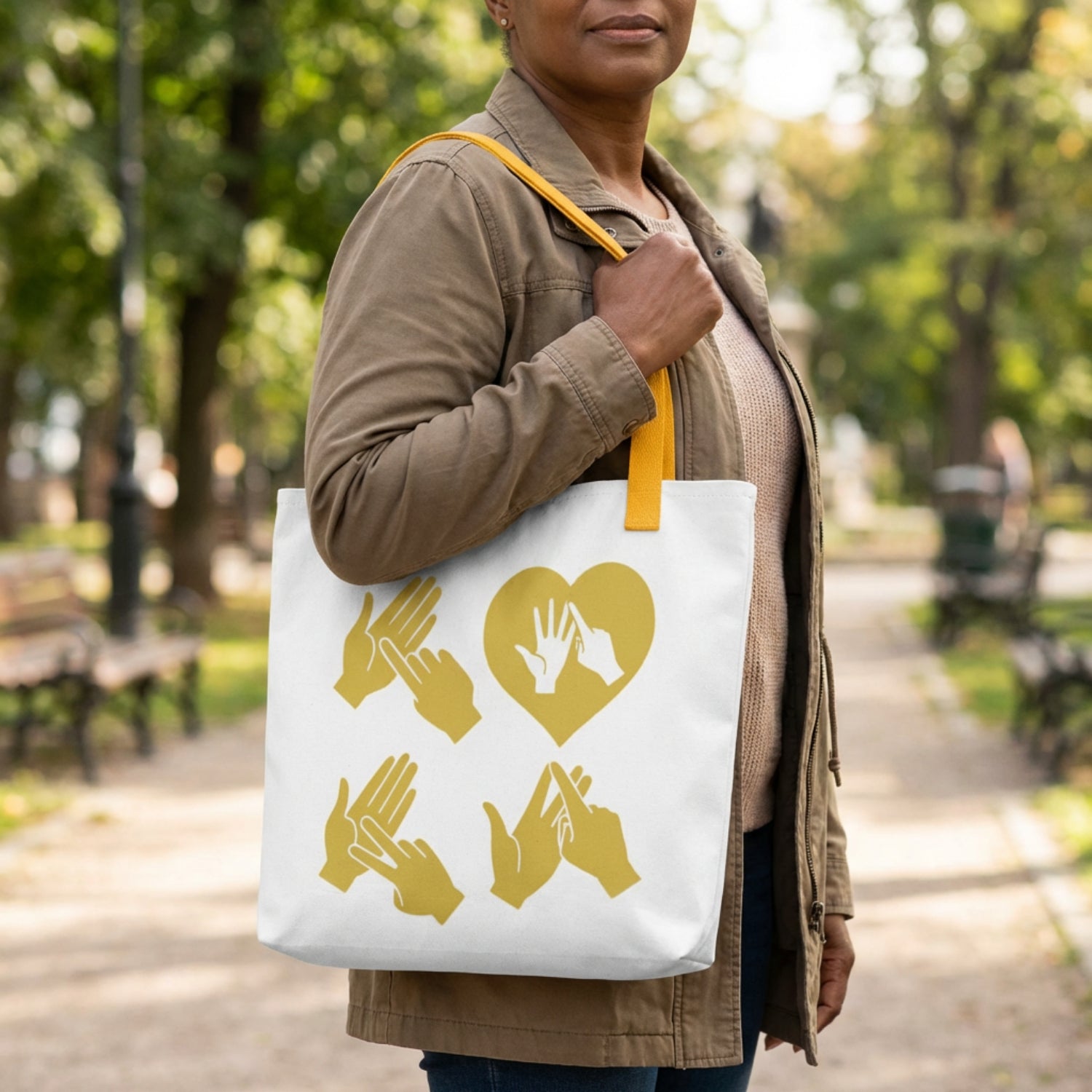 Person holding a tote bag with gold heart and fingerspelling in a park