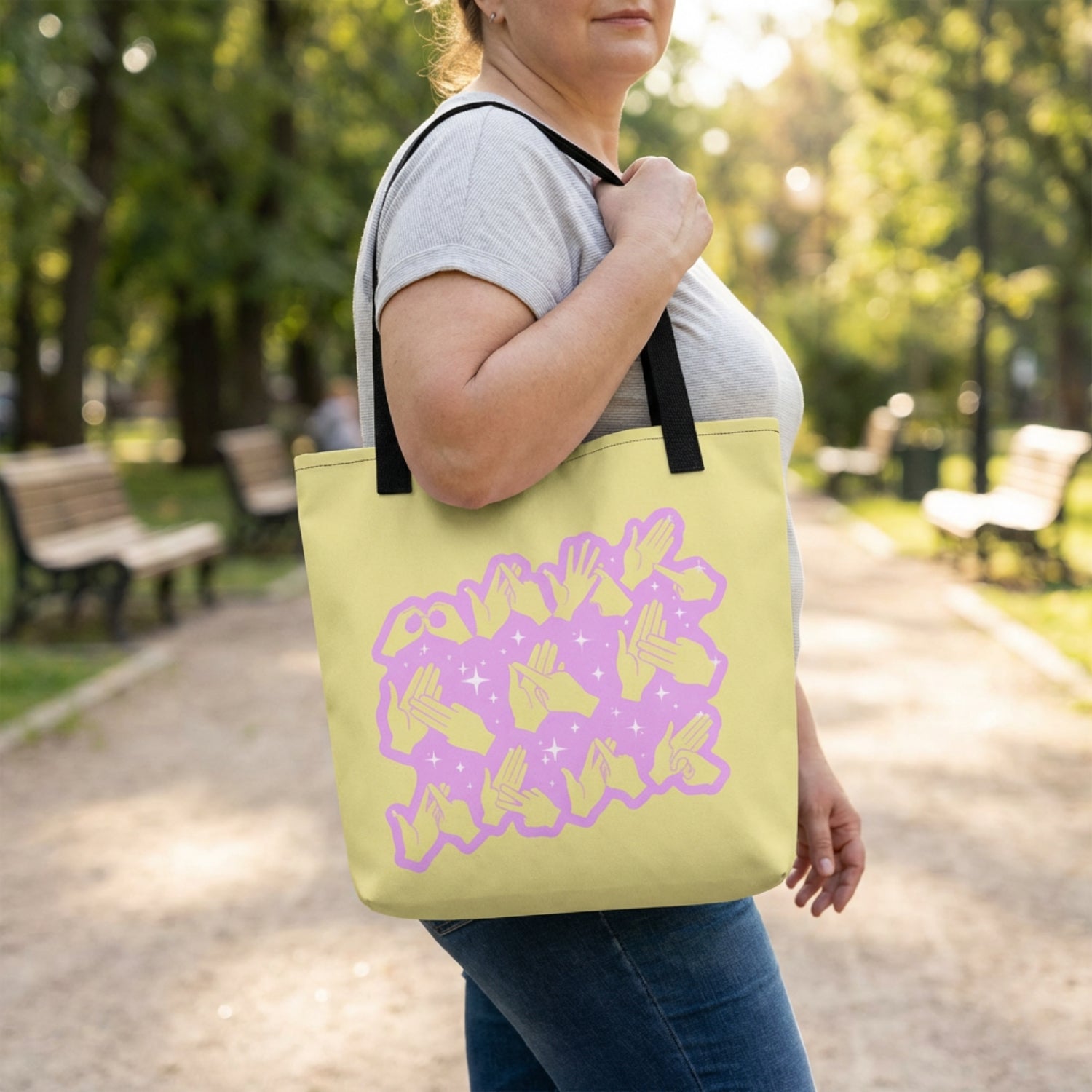 Person holding a yellow tote bag with a purple design in a park