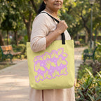 Woman holding a lime green tote bag with a purple design in a park.
