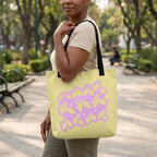 Woman holding a yellow tote bag with a purple design in a park.