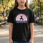 Child wearing a black t-shirt with a graphic design of a dancer and sunset, standing in a park.