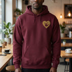 Person wearing a maroon hoodie with a gold heart design in a casual setting