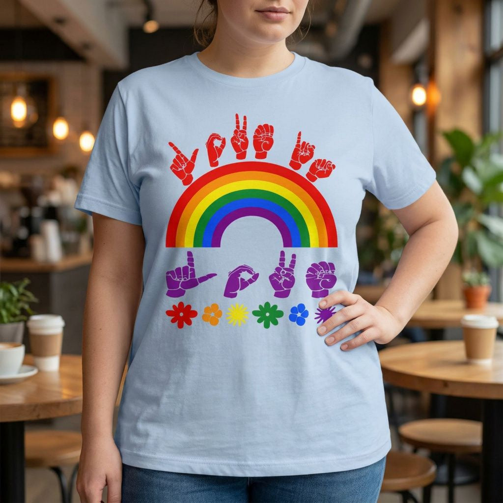 A person wearing a light blue t-shirt with pride rainbow surrounded by the phrase "Love Is Love" in ASL fingerspelling