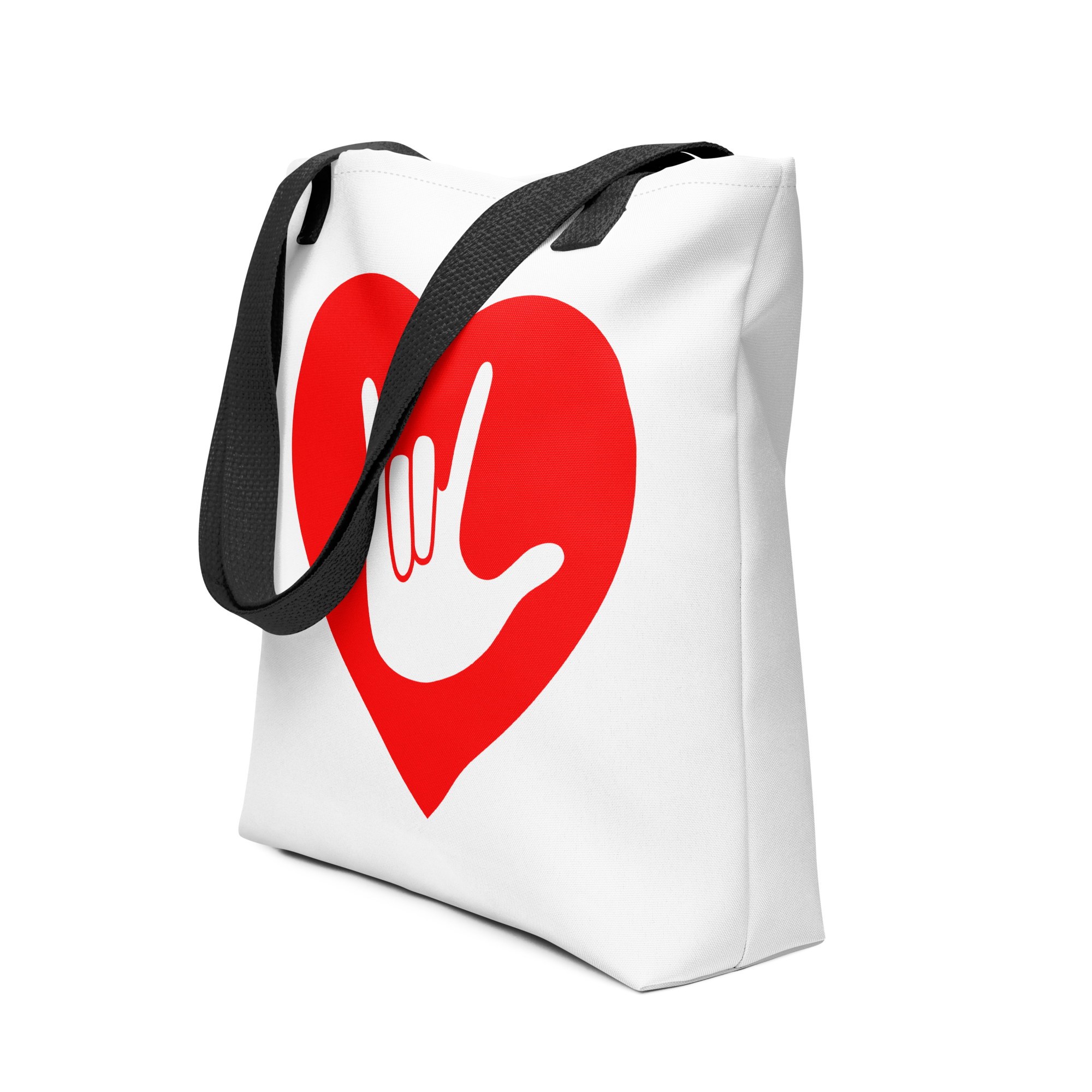 An angled view of a white Tote bag with a black handle and a red heart with the ASL I love you sign at its center.