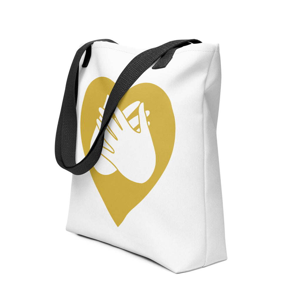 An angled view of a white Tote bag with a black handle and a gold heart with the BSL love sign at its centre.