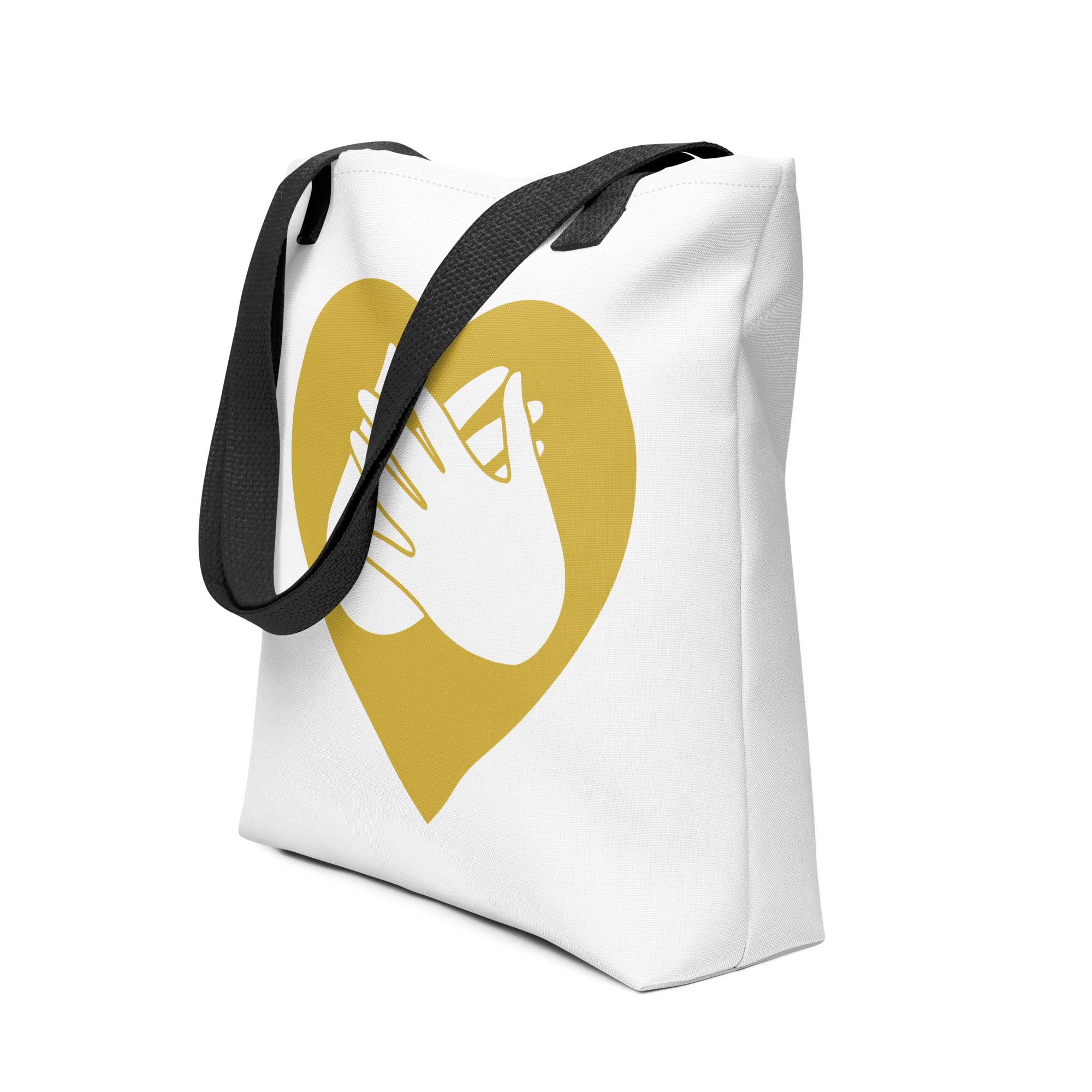 An angled view of a white Tote bag with a black handle and a gold heart with the BSL love sign at its centre.