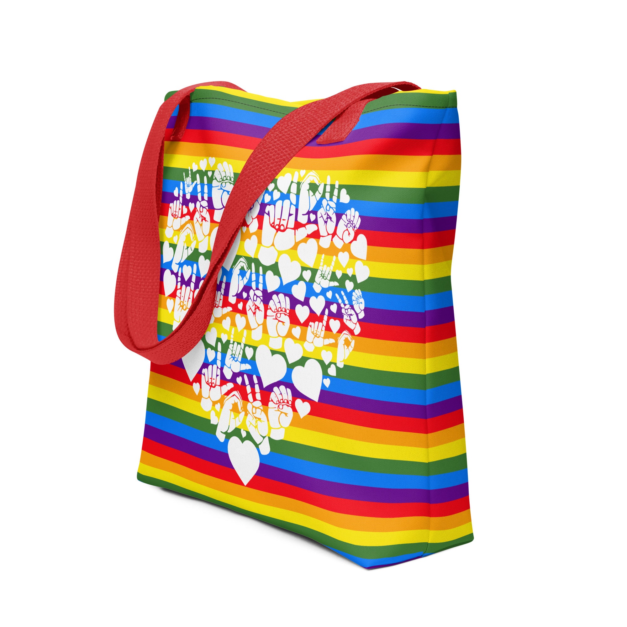 An angled view of a pride rainbow coloured tote bag with a red handle and a white ASL mosaic heart design
