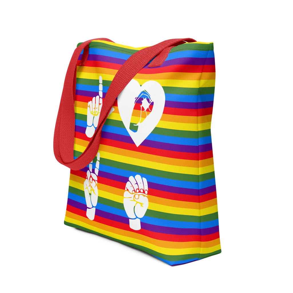 An angled view of a pride rainbow colored tote bag with a red handle and the word LOVE in white ASL fingerspelling design