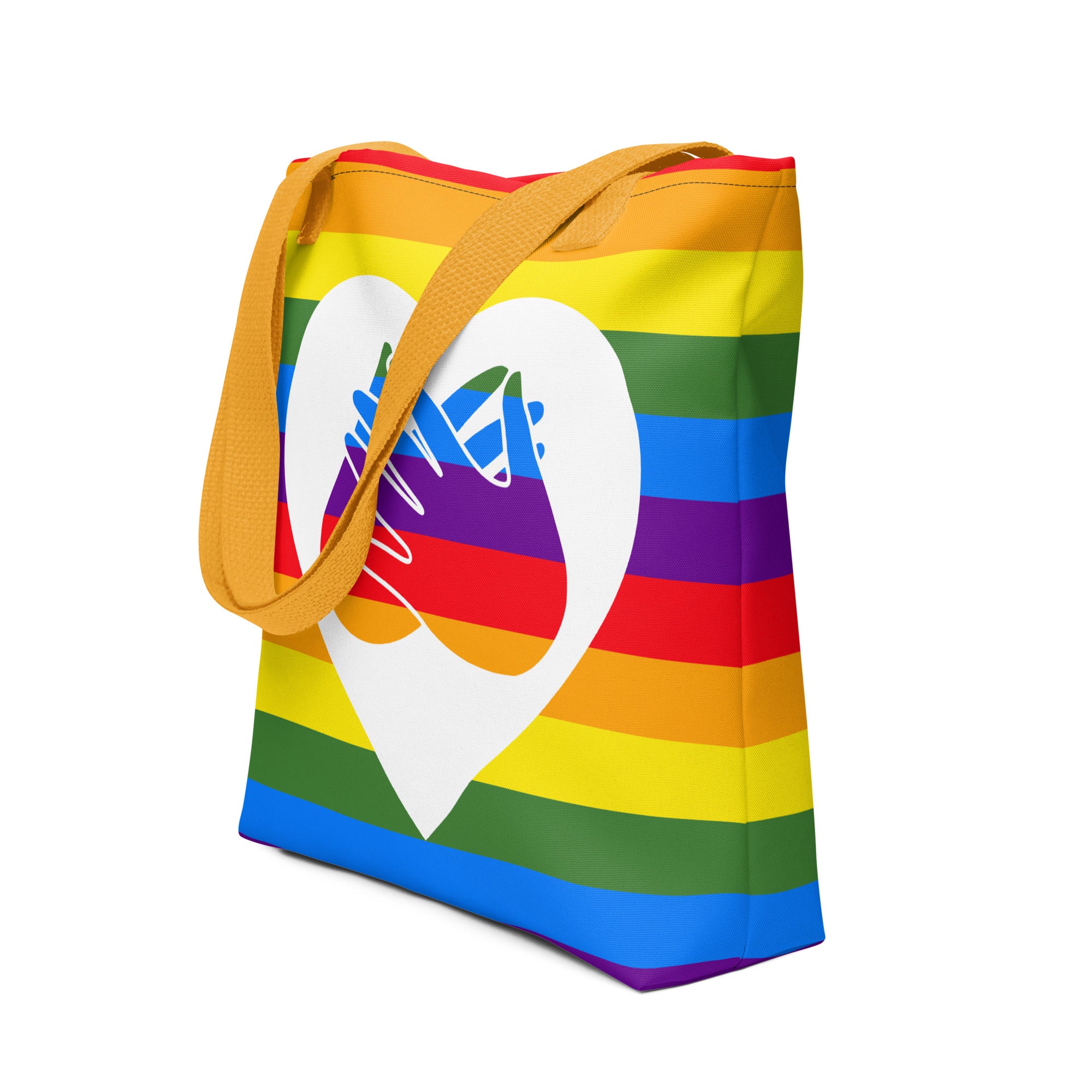 An angled view of a pride rainbow coloured tote bag with a yellow handle and a white heart with the BSL love sign at its centre.