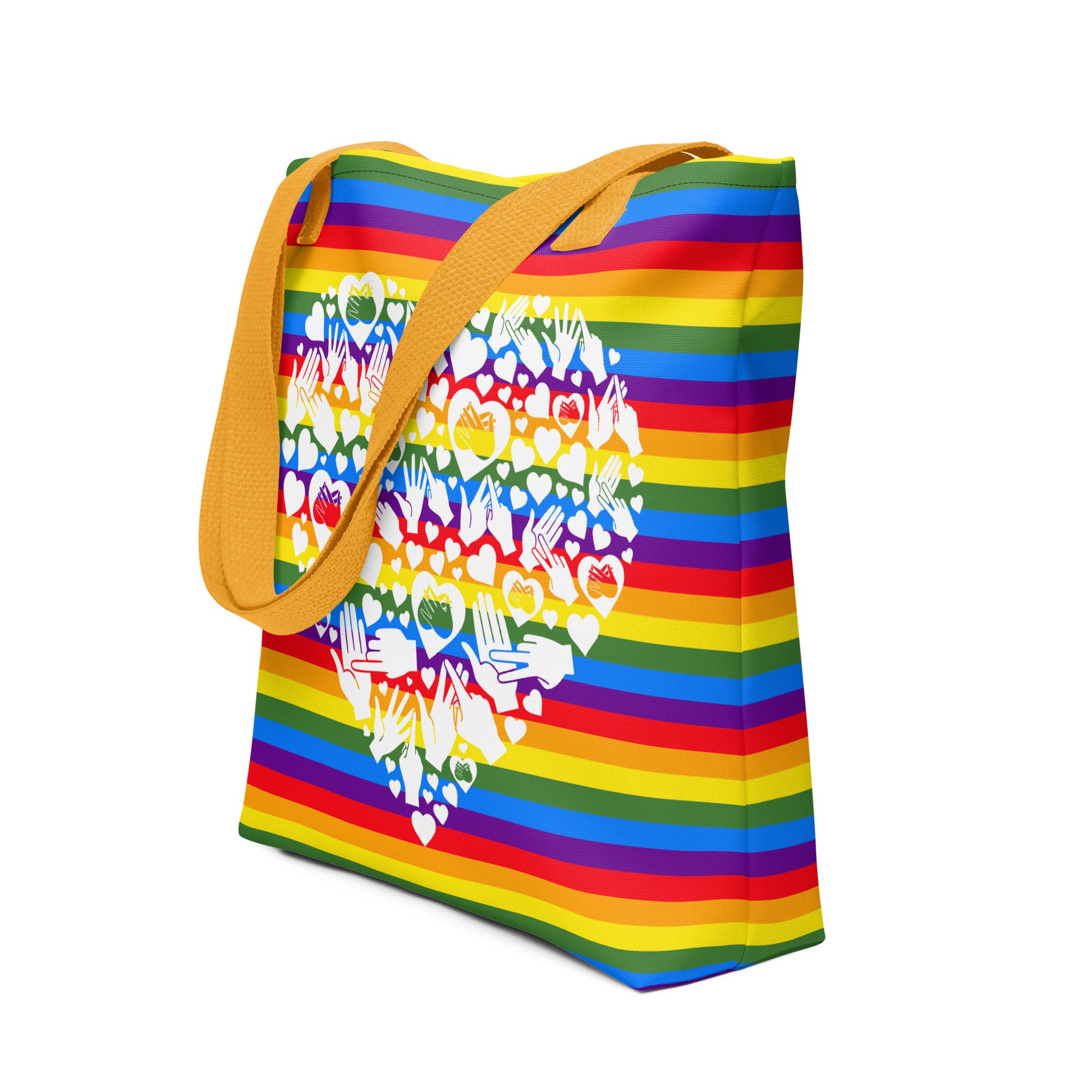 An angled view of a pride rainbow coloured tote bag with a yellow handle and a white mosaic heart design