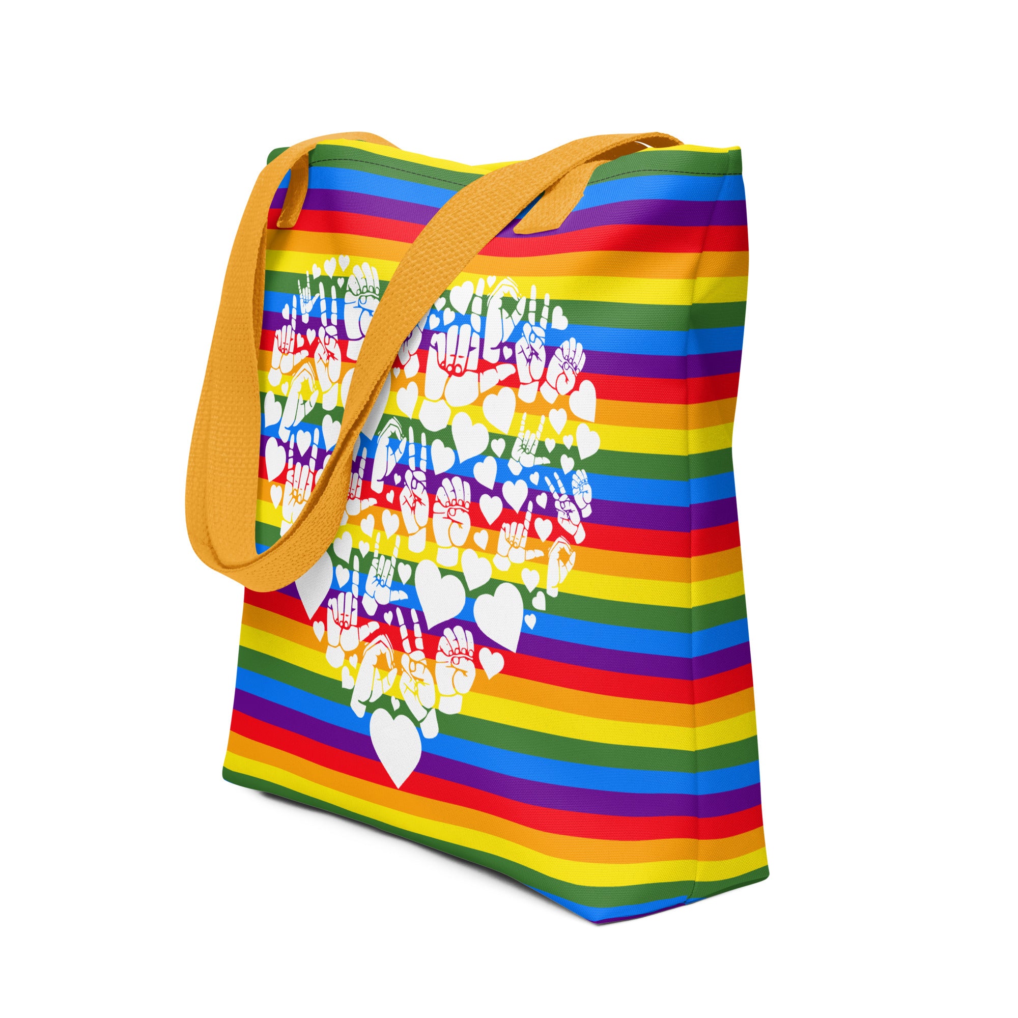 An angled view of a pride rainbow coloured tote bag with a yellow handle and a white ASL mosaic heart design